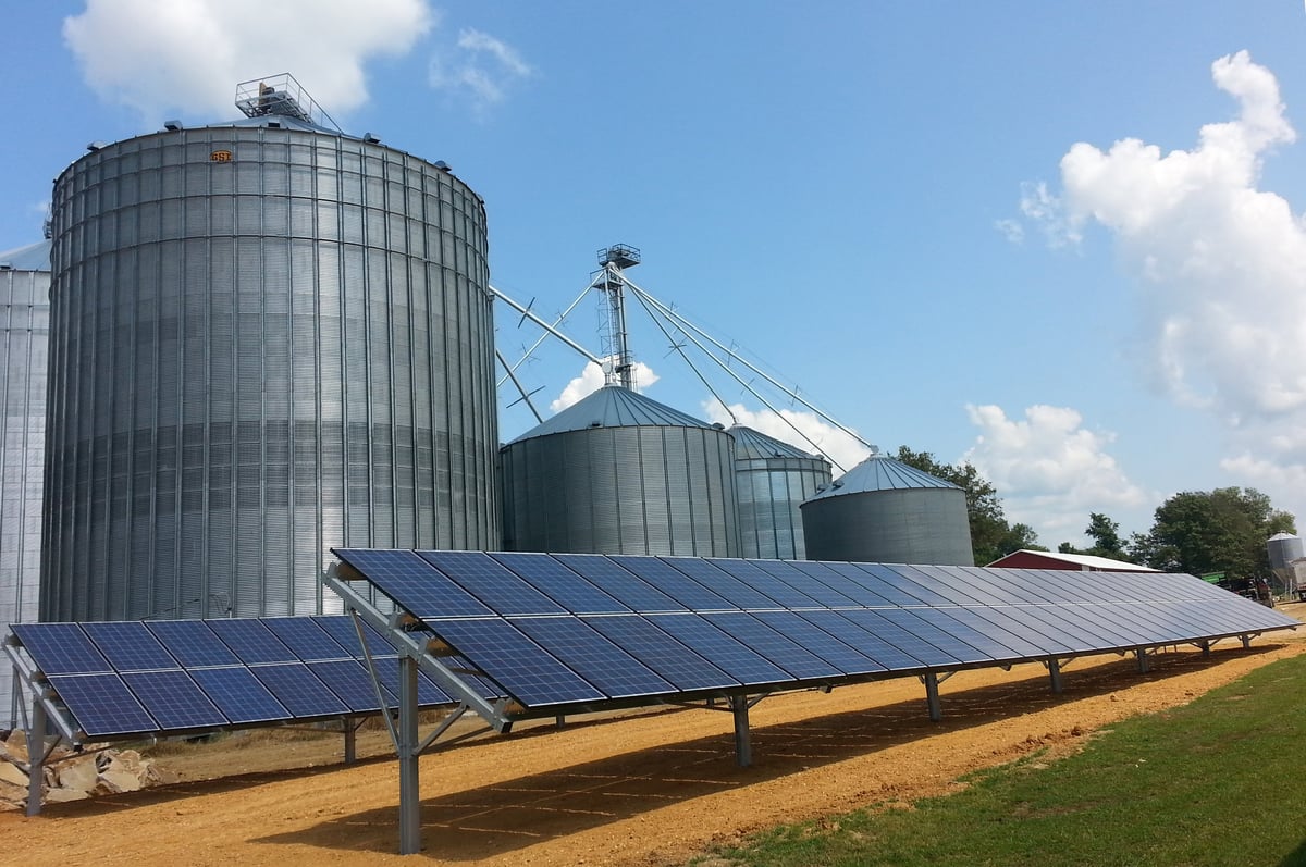 Illinois solar panels next to several silos on a farm.